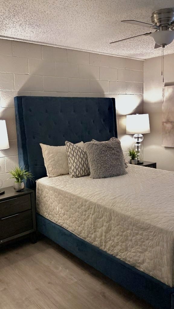 Bedroom with tufted navy headboard, two lamps and ceiling fan