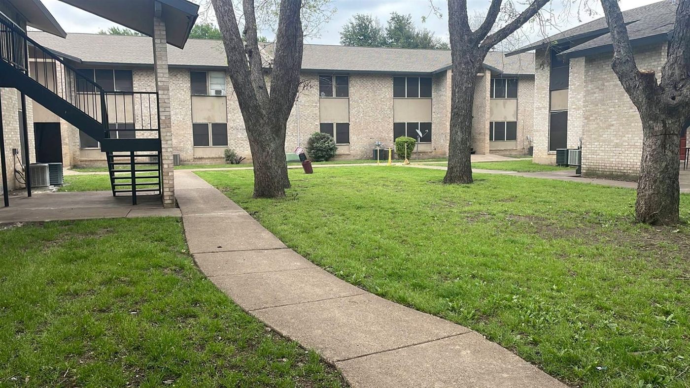 Grassy courtyard with mature trees and a walkway between two-story brick buildings